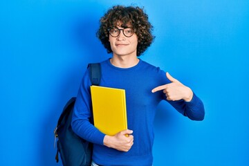 Handsome young man wearing student backpack and holding book pointing finger to one self smiling happy and proud