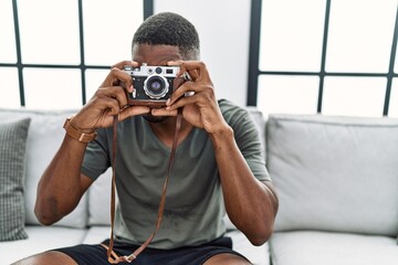 Young african american man smiling confident using vintage camera at home