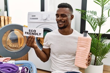 Young african man doing laundry holding eco friendly paper winking looking at the camera with sexy...