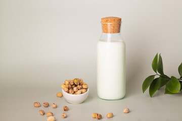 Bottled pistachio milk on a light background with raw nuts and fresh leaves, showcasing dairy alternatives.