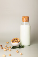 Plant-based milk scene with pistachio milk in a bottle, surrounded by whole nuts and vibrant leaves.