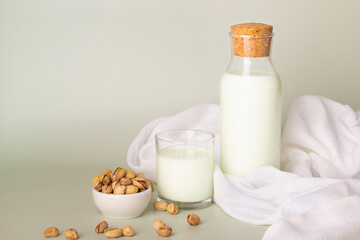 Fresh pistachio milk in a glass bottle and cup, set against a neutral backdrop with scattered pistachios.