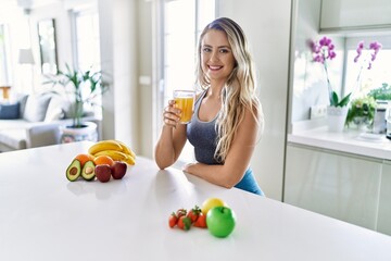 Young caucasian fitness woman wearing sportswear drinking healthy orange juice looking positive and...