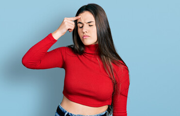 Young brunette teenager wearing red turtleneck sweater pointing unhappy to pimple on forehead, ugly...