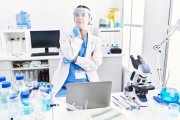 Young hispanic woman wearing scientist uniform serious face thinking about question with hand on chin, thoughtful about confusing idea