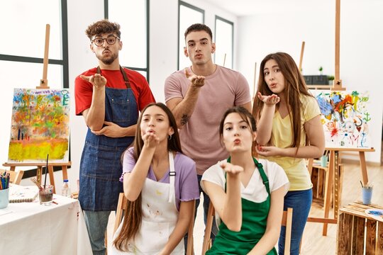Group of five hispanic artists at art studio looking at the camera blowing a kiss with hand on air being lovely and sexy. love expression.