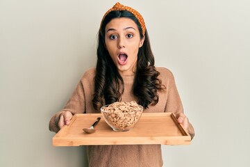 Young hispanic woman holding tray with healthy whole grain cereals afraid and shocked with surprise and amazed expression, fear and excited face.