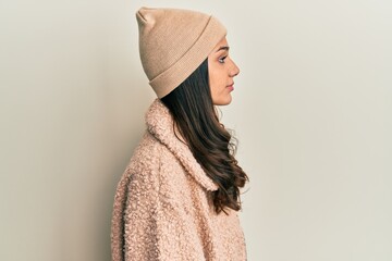Young hispanic woman wearing wool sweater and winter hat looking to side, relax profile pose with...