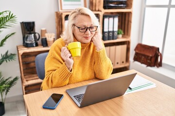 Middle age blonde woman businesswoman drinking coffee working at office