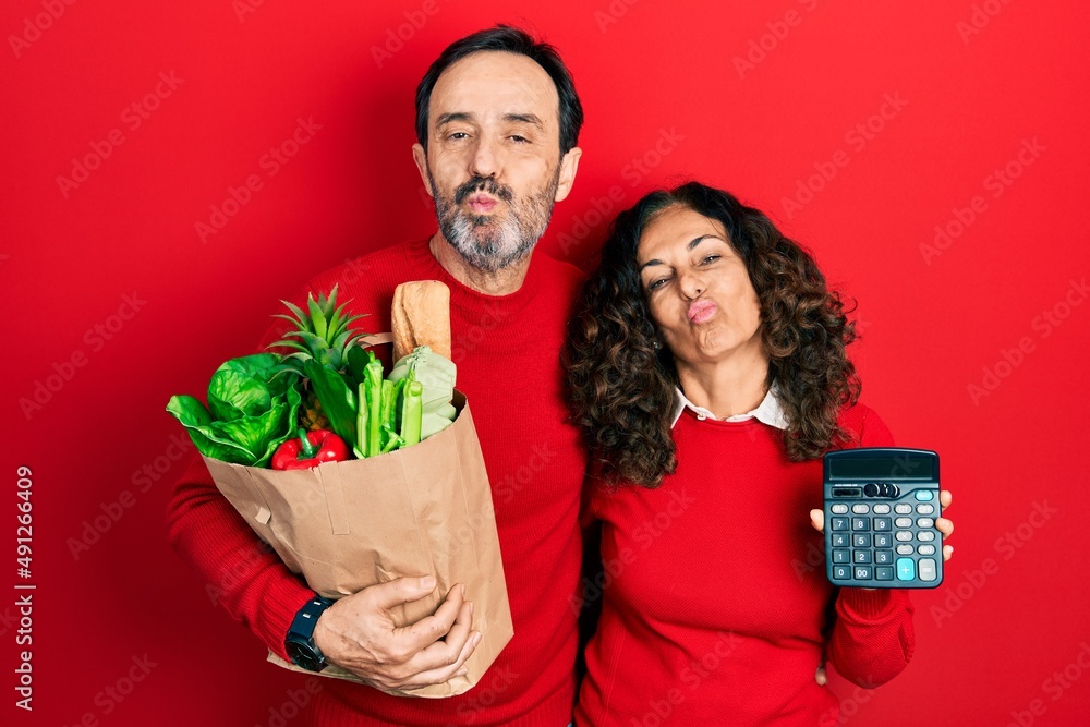 Sticker middle age couple of hispanic woman and man holding groceries bag and calculator looking at the came