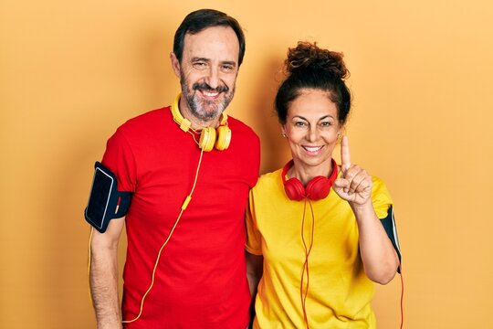 Middle age couple of hispanic woman and man wearing sportswear and arm band showing and pointing up with finger number one while smiling confident and happy.