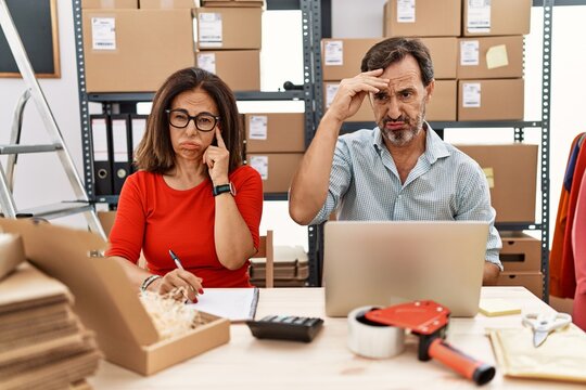 Middle age couple working at small business ecommerce worried and stressed about a problem with hand on forehead, nervous and anxious for crisis