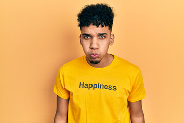 Young african american man wearing t shirt with happiness word message puffing cheeks with funny face. mouth inflated with air, crazy expression.