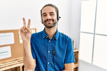 Young hispanic man with beard wearing call center agent headset at the office smiling with happy...
