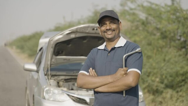 Portriat shot smiling car mechanic stading in front of borken on roadside by looking at camera - concept of mobile car service or support and maintenance