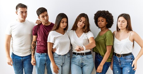 Obraz premium Group of young friends standing together over isolated background checking the time on wrist watch, relaxed and confident