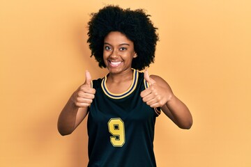 Young african american woman wearing basketball uniform approving doing positive gesture with hand, thumbs up smiling and happy for success. winner gesture.