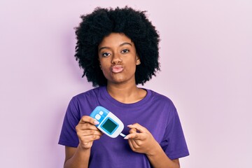 Young african american woman holding glucometer device looking at the camera blowing a kiss being lovely and sexy. love expression.
