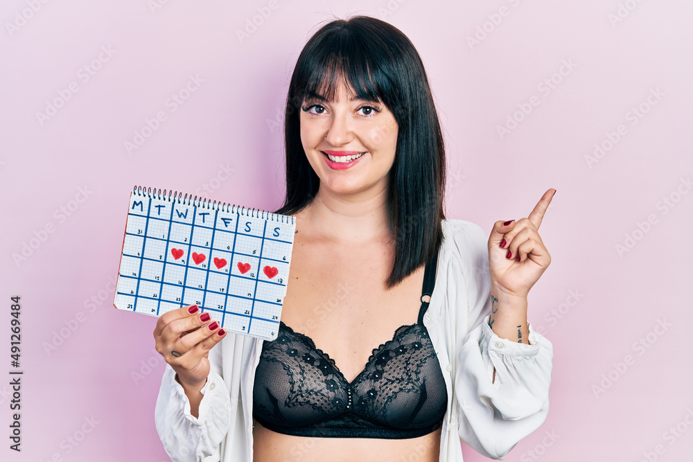 Poster young hispanic woman holding menstrual calendar wearing underwear smiling happy pointing with hand a