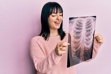Young hispanic woman holding chest x-ray winking looking at the camera with sexy expression,...