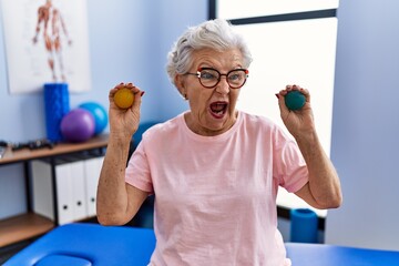 Senior woman with grey hair holding hands strength balls angry and mad screaming frustrated and furious, shouting with anger. rage and aggressive concept.