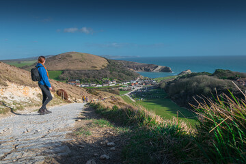 Girl in blue hoodie and with the black backpack looks on the Lulworth Cove, Jurassic Coast, Dorset, UK - obrazy, fototapety, plakaty