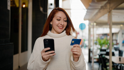 Fototapeta na wymiar Young redhead woman using smartphone and credit card at street
