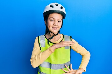 Beautiful brunette little girl wearing bike helmet and reflective vest gesturing with hands showing big and large size sign, measure symbol. smiling looking at the camera. measuring concept.
