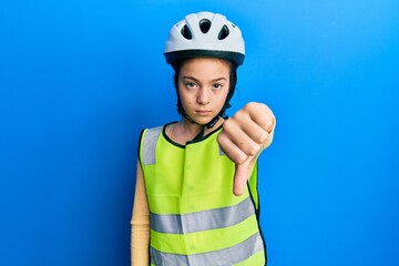 Beautiful brunette little girl wearing bike helmet and reflective vest looking unhappy and angry showing rejection and negative with thumbs down gesture. bad expression.