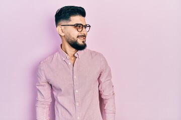 Handsome man with beard wearing casual shirt and glasses looking away to side with smile on face, natural expression. laughing confident.