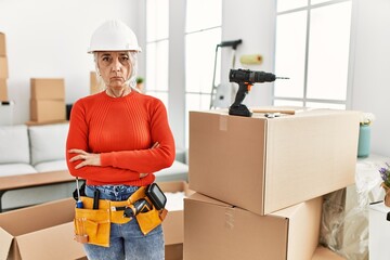 Middle age grey-haired woman wearing hardhat standing at new home skeptic and nervous, disapproving expression on face with crossed arms. negative person.