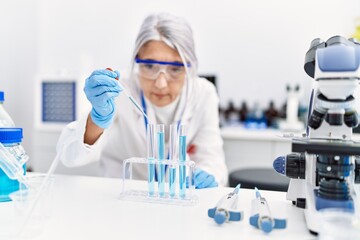 Middle age grey-haired woman wearing scientist uniform using pipette at laboratory