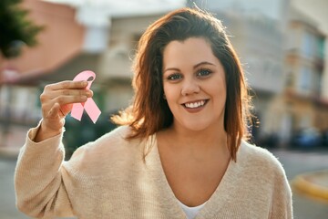 Young irish plus size girl smiling happy holding pink cancer ribbon at the city.