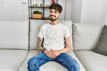 Young hispanic man smiling happy sitting on the sofa at home.