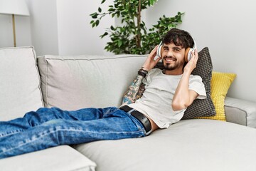 Young hispanic man listening to music lying on the sofa at home.