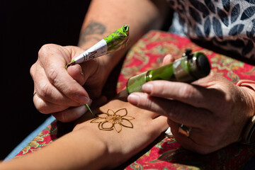 A Henna artist applies a floral decoration to a woman's hand during a pre-wedding ceremony which is...
