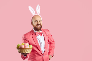 Studio shot of happy bald young man with ginger beard, wearing pink suit, bow tie and funny bunny...