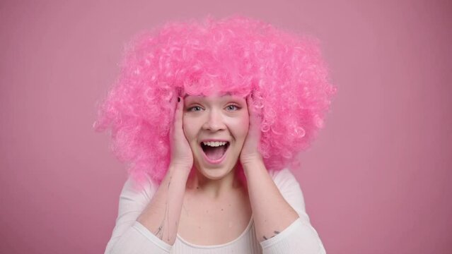 Surprised woman in fancy wig. Portrait of joyful young female in huge pink wig.