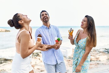 Three young hispanic friends smiling happy eating ice cream at the beach.
