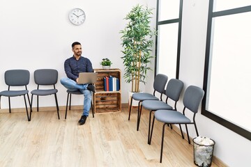 Young hispanic man using laptop sitting on chair at waiting room