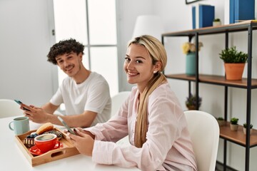 Fototapeta premium Young couple having breakfast using smartphone at home.