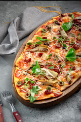 Vegetarian long pizza with artichokes, dried tomatoes, olives and basil on a gray concrete background. Italian dish pizza made of dough with vegetables, close up