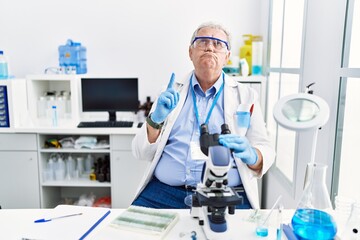 Senior caucasian man working at scientist laboratory pointing up looking sad and upset, indicating direction with fingers, unhappy and depressed.