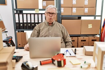 Senior caucasian man working at small business ecommerce with laptop making fish face with lips, crazy and comical gesture. funny expression.