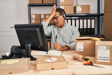 Senior man working at small business ecommerce wearing headset surprised with hand on head for...