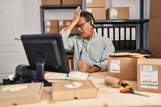 Senior man working at small business ecommerce wearing headset surprised with hand on head for mistake, remember error. forgot, bad memory concept.