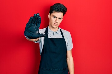 Young hispanic man wearing apron doing stop sing with palm of the hand. warning expression with...