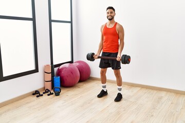 Young arab man smiling confident training with dumbbells at sport center