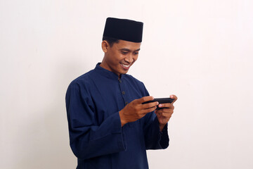 Young Asian Muslim man wearing muslim clothes holding mobile phone look at phone screen