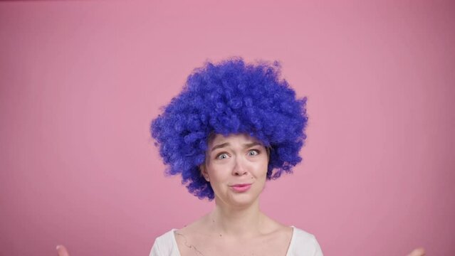 Portrait of shocked woman on pink background. Young female in blue wig has her head boiled.
